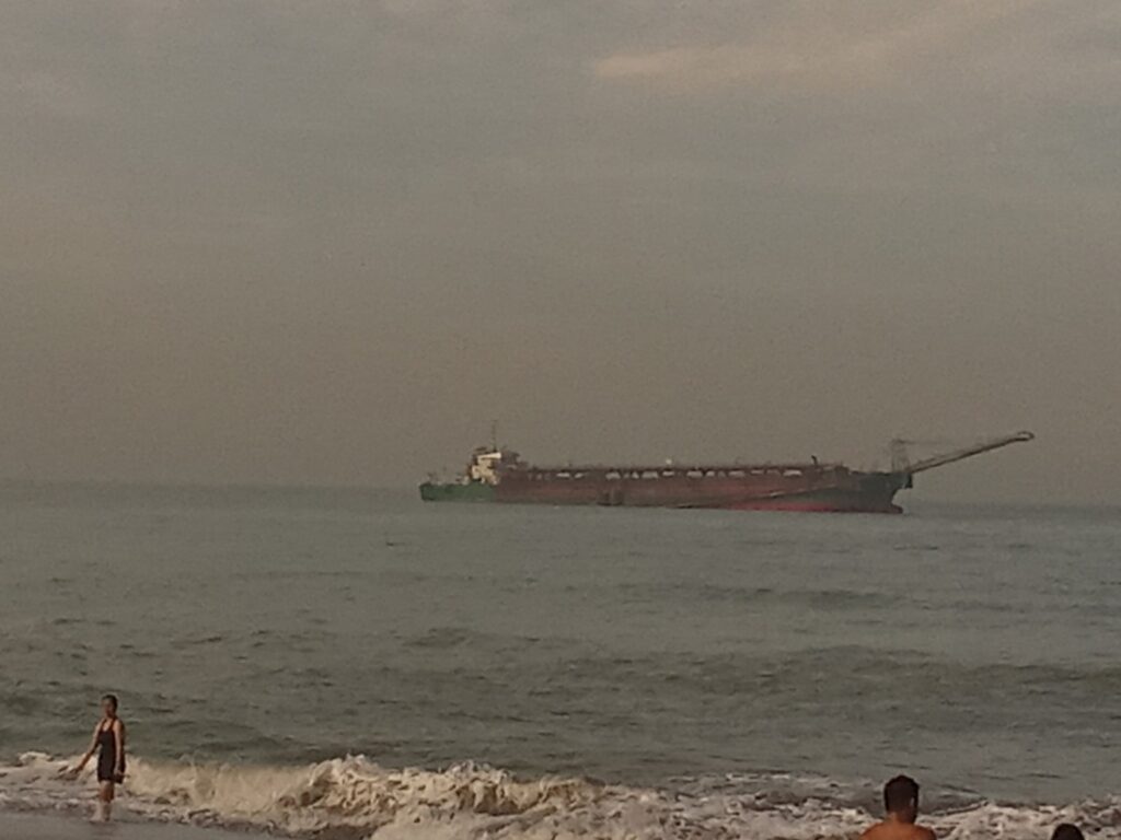 Draga al lavoro poco al largo di una spiaggia con la costa bassa sullo sfondo
