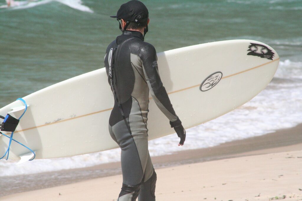 Surfista in muta lunga con cappuccio che entra in acqua in una mattina d'inverno