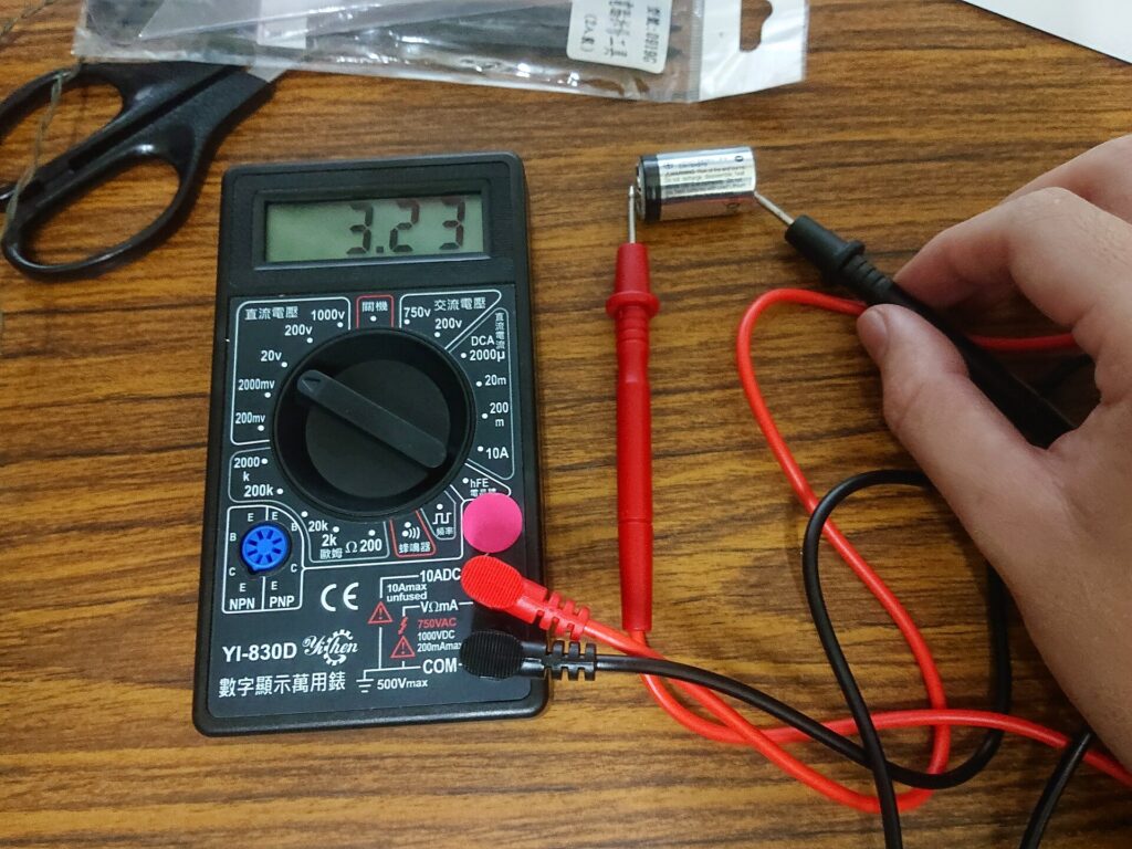 Multimetro appoggiato su una batteria mentre si misura la tensione ai morsetti